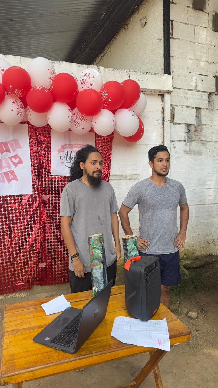 Dos facilitadores junto a una mesa de apoyo y decoración del Día de la Madre